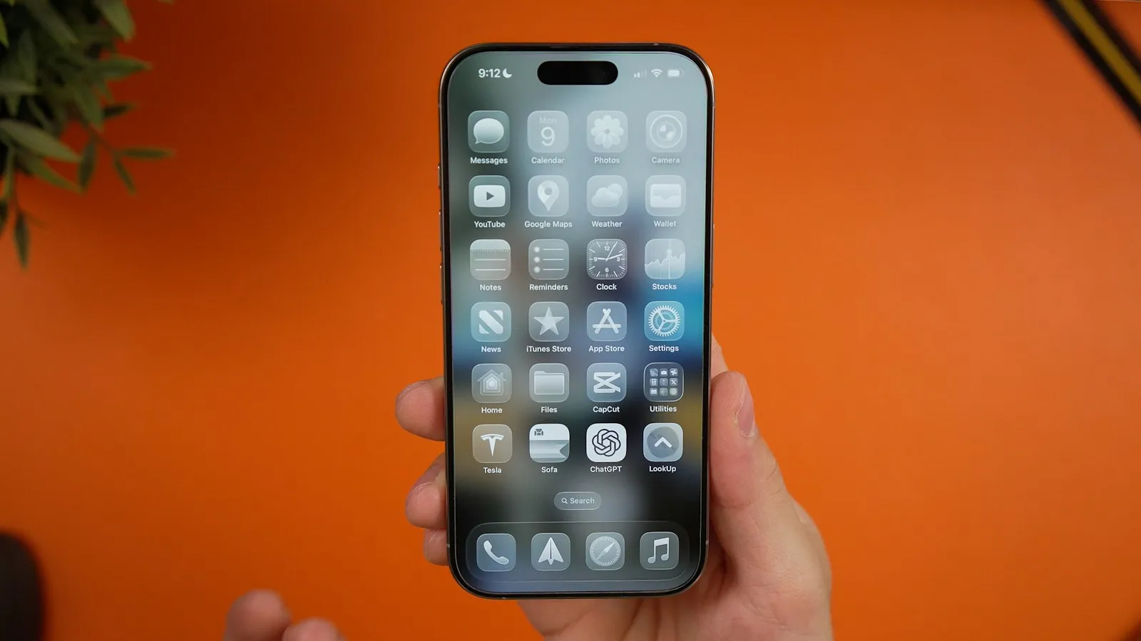 Una mano sujeta un iPhone con la pantalla de inicio llena de apps, sobre un fondo naranja